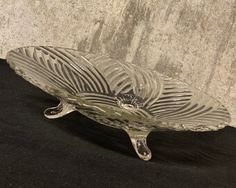 May include: A clear glass pedestal bowl with a fluted design and three legs. The bowl is on a black surface.