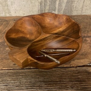 May include: A wooden serving bowl with three sections, shaped like a leaf, with a set of nutcrackers inside.