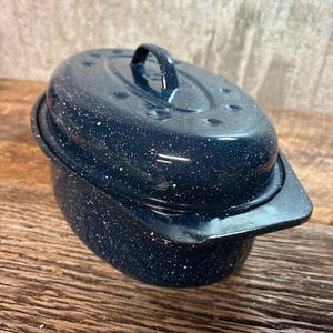 May include: A navy blue enamelware oval roaster with a lid and handle. The roaster has a speckled white pattern and sits on a wooden surface. The lid has a handle and several small holes.