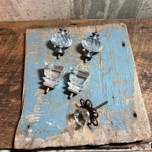 May include: Five decorative cabinet knobs including two clear glass knobs with silver-toned metal bases, two clear faceted glass knobs with silver-toned metal bases, and one clear glass knob with a dark red metal flower-shaped backplate.