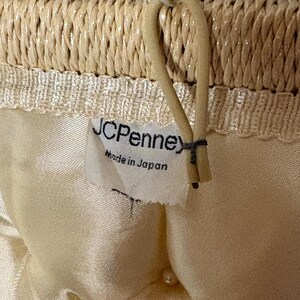 May include: Close-up of a woven straw handbag. The top edge is a tightly woven straw, with a cream-colored satin interior. A tag reads "JCPenney Made in Japan". A beige handle is attached to the top.