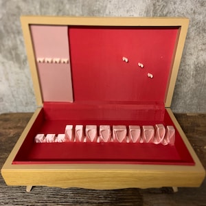 May include: A wooden jewelry box with a red interior and a pink velvet lining. The box has a hinged lid and a small compartment for storing jewelry. The box is decorated with a floral design.