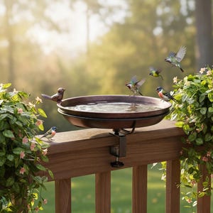May include: A circular, dark brown bird bath basin mounted to a wooden deck railing with a black metal C-clamp. The basin is filled with water and surrounded by several small, colorful birds, including one perched on the rim and others in flight.