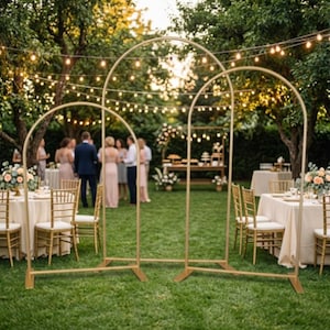 Può includere: Un set di due telai ad arco in metallo color oro con cime arrotondate, ciascuno supportato da una base rettangolare. Le strutture sono realizzate in sottile metallo tubolare e sono progettate per stare in piedi su una superficie piana.
