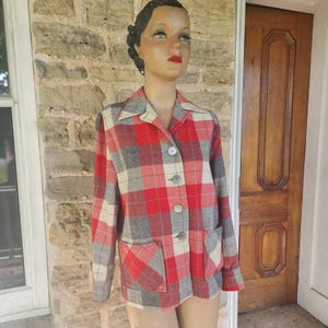 May include: A long-sleeved button-down jacket featuring a red, gray, and cream plaid pattern. The garment includes a classic collar, four visible buttons down the front, and two square patch pockets positioned at the lower front section.