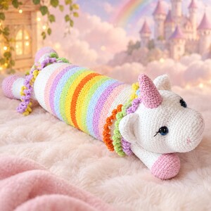 May include: A crochet unicorn plush toy featuring a long, cylindrical body with horizontal stripes in rainbow colors. The head is white with a pink horn, blue eyes, and a mane made of colorful, curly yarn. The tail is also curly and multicolored.