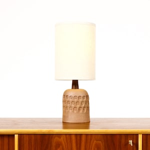 May include: A mid-century modern table lamp with a brown ceramic base featuring a repeating pattern of circles. The lamp has a white fabric shade.
