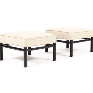 May include: Two square ottomans with a beige fabric upholstery and black wooden frames.