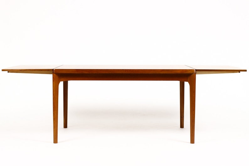 May include: A wooden extendable dining table with a light brown finish. The table has a rectangular top and four legs. The table is shown with the leaves extended.