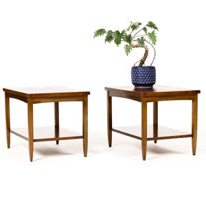 May include: Two wooden end tables with a lower shelf. The tables are brown and have a simple, mid-century modern design.