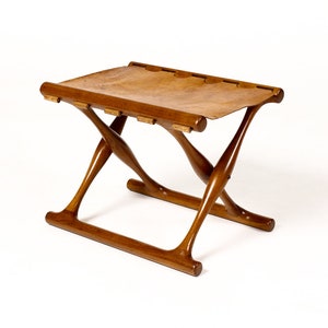 May include: A wooden folding stool with a brown leather seat. The stool has a simple, elegant design and is perfect for a variety of settings.
