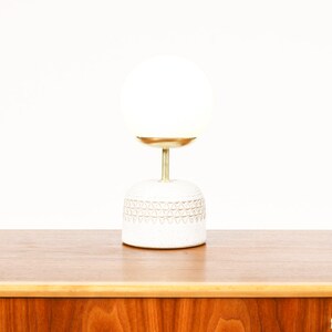 May include: A white ceramic table lamp with a gold base and a white glass globe shade.