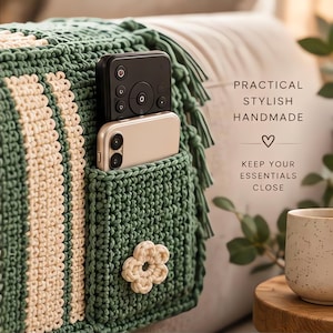 May include: A dark green crocheted sofa armrest organizer with cream-colored vertical stripes and a small cream flower accent. It features a pocket holding a black remote control and a gold smartphone. Text reads: PRACTICAL STYLISH HANDMADE KEEP YOUR ESSENTIALS CLOSE.