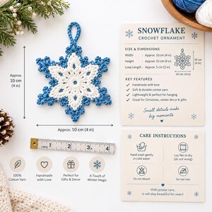May include: A white and blue crochet snowflake ornament with a hanging loop. A measuring tape shows a width and height of approximately 4 inches. The accompanying text card details the snowflake crochet ornament dimensions and care instructions.