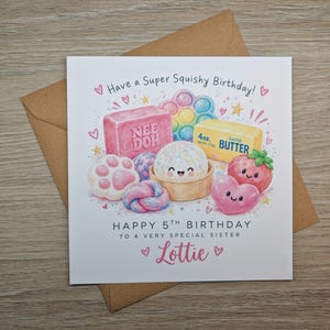 May include: A square birthday card featuring a colorful illustration of squishy toys, including a pink Nee Doh block, a rainbow pop-it, a stick of butter, and cute characters. Text reads: Have a Super Squishy Birthday! HAPPY 5TH BIRTHDAY TO A VERY SPECIAL SISTER Lottie.