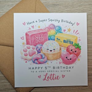 May include: A square birthday greeting card with a brown envelope. The card features watercolor illustrations of a pink Nee Doh block, a pop-it toy, a stick of 4oz salted butter, a cat paw, a strawberry, and a heart, with the text Have a Super Squishy Birthday! HAPPY 5TH BIRTHDAY TO A VERY SPECIAL SISTER Lottie.