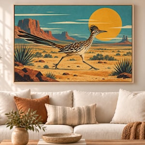 May include: A rectangular wall art print in a light wood frame featuring a desert landscape illustration. A roadrunner bird runs across the sandy ground with mesas, cacti, and a large yellow sun set against a teal sky in the background.
