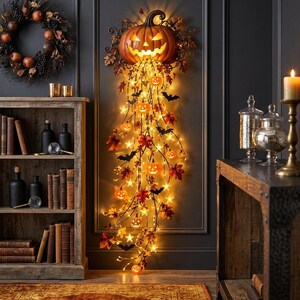Op de afbeelding: Een wanddecoratie voor Halloween met een grote, verlichte pompoen aan de bovenkant, met trapsgewijze ranken versierd met kleinere gloeiende pompoenen, stervormige lichtjes, herfstbladeren en zwarte silhouetten van vleermuizen.