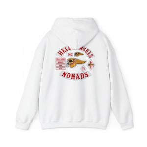 May include: A white hooded sweatshirt featuring a large back graphic with the text HELLS ANGELS NOMADS. The design includes a winged skull emblem, red lettering, and diamond-shaped patches with the text 1% and MC, all printed in red, yellow, and black.
