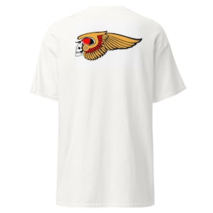 May include: A white short-sleeve t-shirt featuring a graphic on the back. The design depicts a white skull wearing a gold-colored winged helmet with red accents. The wings are stylized with black outlines and extend horizontally across the upper back.