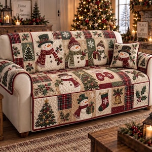 May include: A quilted sofa cover featuring a patchwork design with snowmen, Christmas trees, holly, stockings, and bells in red, green, and cream colors. The cover includes a matching square throw pillow with a snowman graphic and plaid accents.