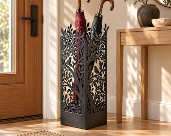 May include: A tall, rectangular black metal umbrella stand featuring an intricate laser-cut design of tree branches, leaves, and small birds. The stand holds two umbrellas, one with a deep red canopy and one with a black canopy, both with curved handles.
