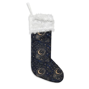 May include: A Christmas stocking featuring a dark navy blue fabric printed with a celestial pattern of golden crescent moons, swirling galaxies, and white star constellations. The top cuff is made of thick, white, fluffy faux fur material.