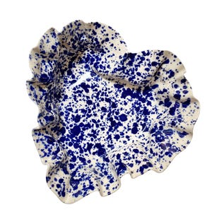 May include: A white ceramic serving dish with a ruffled edge and a blue splatter pattern. The dish has a unique, organic shape and is suitable for serving food or as a decorative piece.