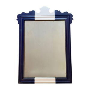 May include: A rectangular mirror with a navy blue frame and a white stripe across the top and bottom. The mirror has a decorative, scalloped top. The mirror's reflective surface is a light gold color.