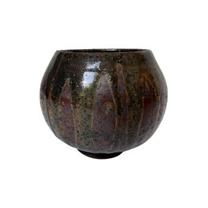 May include: A round ceramic bowl with a dark brown and black speckled glaze. The exterior features a series of vertical, elongated oval indentations that create a textured pattern around the circumference of the vessel, ending at a small base.