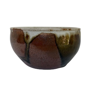 May include: A ceramic bowl with a rounded shape, featuring a deep reddish-brown base color that transitions into a dark olive green tone. The upper rim is finished with a thick, creamy white glaze that drips down the sides in a vertical pattern.