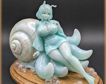 May include: A pale mint green figurine of a character with antennae, wearing a short garment with circular patterns, resting against a large, pearlescent snail shell. The figure is surrounded by small, clear, spherical bubbles on a wooden base.