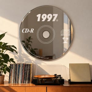 May include: A circular wall mirror designed to resemble a compact disc. The reflective surface features white printed text including 1997, CD-R, the Compact Disc Digital Audio logo, a palm tree icon, and the phrase For all yousers - Be mindful not to lose your own identity and values.