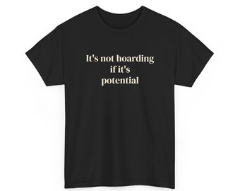 Puede incluir: Una camiseta negra de manga corta con el texto en blanco It's not hoarding if it's potential centrado en el pecho. La prenda tiene un cuello redondo clásico y un dobladillo recto, ofreciendo un aspecto sencillo y limpio para el uso diario.