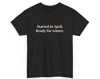 Puede incluir: Una camiseta negra de manga corta con el texto en blanco "Started in April. Ready for winter." centrado en el pecho. La prenda tiene cuello redondo y un corte estándar, confeccionada en tela negra lisa con letras claras y legibles.