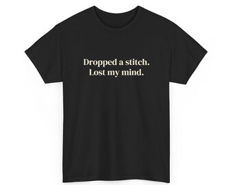 Puede incluir: Una camiseta negra de manga corta con el texto "Dropped a stitch. Lost my mind." impreso en color crema claro en el centro del pecho. La prenda tiene un cuello redondo y un corte estándar con mangas cortas.