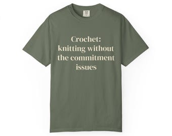 Puede incluir: Una camiseta de manga corta de color verde oliva con el texto en color crema "Crochet: knitting without the commitment issues" impreso en el centro del pecho. La camiseta tiene cuello redondo y un corte estándar con etiqueta visible.