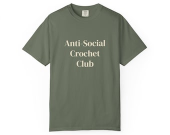 Puede incluir: Una camiseta de manga corta de color verde oliva con el texto Anti-Social Crochet Club impreso en color crema claro en el centro del pecho. La prenda tiene cuello redondo y un corte estándar con una etiqueta de marca visible en el cuello.
