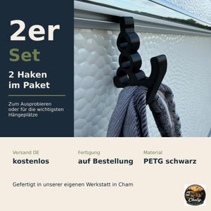 May include: A black plastic hook designed to slide onto a rail, featuring a vertical structure with three circular cutouts and a curved arm for hanging items. The text 2er Set, 2 Haken im Paket, Zum Ausprobieren oder f&uuml;r die wichtigsten H&auml;ngepl&auml;tze is visible.