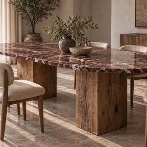 May include: An oval dining table with a polished deep red marble top featuring white veining, supported by two thick, rectangular rustic wooden pedestals. The table is surrounded by several chairs with light beige textured fabric seats and wooden legs.