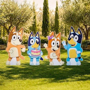 May include: Four colourful cartoon dog character cutouts standing in a row. The figures include two blue and two orange dogs, with one holding a pink birthday cake with lit candles and another wearing a small purple bow on its head.