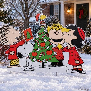May include: A Peanuts holiday yard sign featuring Charlie Brown, Snoopy, Woodstock, Sally, and Lucy decorating a green Christmas tree with red apples and candy canes. The characters are illustrated in their classic style with bold black outlines.