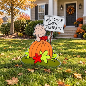 May include: A garden sign featuring a cartoon character with black hair and a red striped shirt leaning on a large orange pumpkin. The character holds a white rectangular sign with black text that reads WELCOME GREAT PUMPKIN. The base is green.