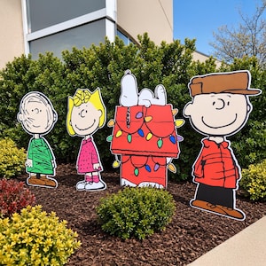 Peut inclure: Un ensemble de quatre panneaux de jardin représentant des personnages de dessin animé : une personne en chemise verte, une personne en robe rose avec un nœud jaune, un chien blanc sur une niche rouge ornée de guirlandes lumineuses et un manteau rouge.