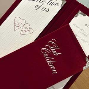 May include: A deep red velvet menu folder with silver corner accents. The cover features the white text Club Calderon. Inside, a white card displays the text The two of us above two heart outlines containing the letters S and F.