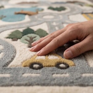 May include: A tufted area rug featuring a textured road map design with a light blue lake, dark green trees, and a yellow car. The rug has a cream-colored base with gray roads, white dashed lane markings, and raised, soft-touch fabric elements.