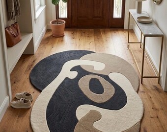 May include: An oval area rug featuring an abstract, organic pattern in shades of charcoal gray, cream, and beige. The rug has a textured surface with carved, wavy lines in the dark gray sections and a plush, tufted pile throughout the design.
