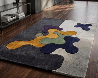 May include: A rectangular area rug featuring a multi-colored abstract pattern with organic, fluid shapes in shades of mustard yellow, sage green, deep purple, and navy blue, set against a background of dark charcoal and light gray sections.