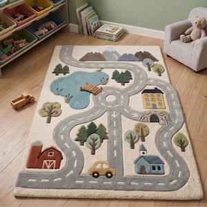 May include: A rectangular area rug featuring a cream-colored background with a textured, raised-pile design of a winding gray road, a blue lake with a wooden bridge, green trees, snow-capped mountains, a yellow house, a barn, and a car.