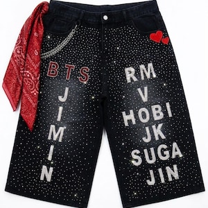 Op de afbeelding: Zwarte denim short met verspreide strass-steentjes, een zilveren ketting en een rode bandana aan de tailleband. De tekst BTS, JIMIN, RM, V, HOBI, JK, SUGA en JIN is gevormd met strass-steentjes, met twee rode hartvormige patches rechtsboven.